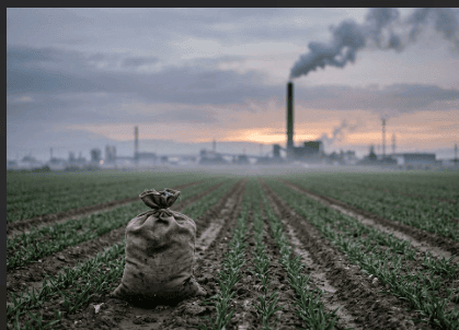 Un campo de cultivo con un saco de fertilizante, al fondo una chimenea industrial